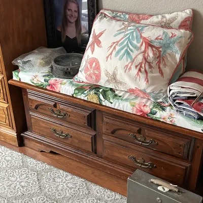 Vintage dark wood bench with four drawers and a floral cushion, topped with throw pillows and decorative items.