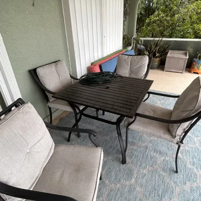 Five-piece outdoor patio dining set, including a dark slatted table and four matching armchairs with light gray cushions.