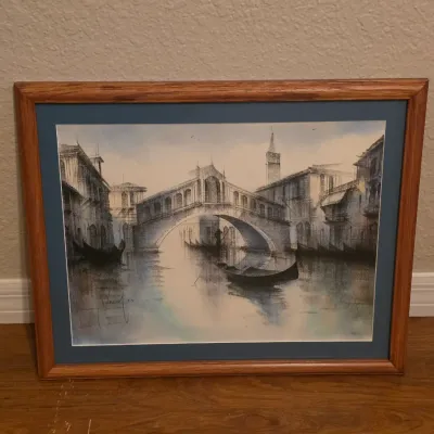 Framed architectural watercolor print depicting gondolas beneath the Rialto Bridge in Venice, set in a blue mat and oak wood frame.