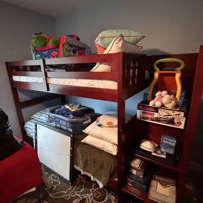 Dark wood twin bunk bed unit featuring built-in side shelving, displayed with bedding, plush toys, and boxed Lionel Flyer train sets.