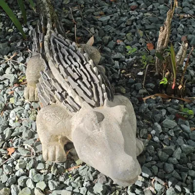 Concrete alligator or crocodile garden statue with a textured slate-style back, resting on a gravel ground cover.