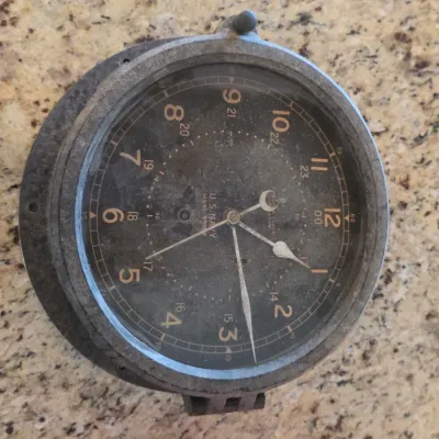 Vintage U.S. Navy bulkhead clock by Chelsea Clock Co., featuring a black 24-hour dial in a heavy metal casing with visible patina.