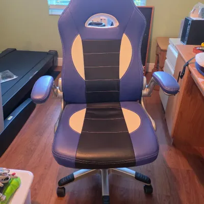 Modern racing-style gaming desk chair featuring blue, black, and white faux leather upholstery, flip-up armrests, and a silver-finished...