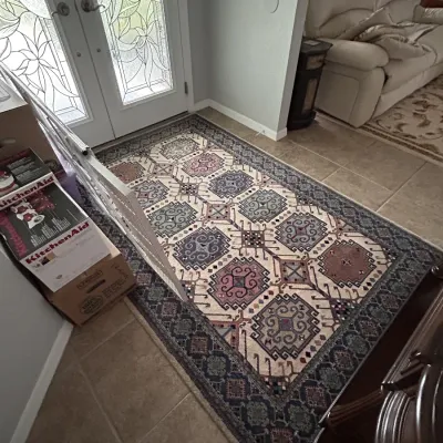 Traditional patterned area rug featuring geometric motifs in shades of cream, blue, and mauve, positioned on tile flooring near an entryway.