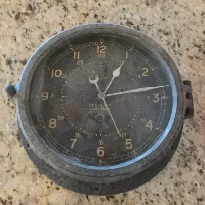 Vintage U.S. Navy bulkhead clock by Chelsea Clock Co., featuring a black 24-hour dial in a heavy metal casing with visible patina.