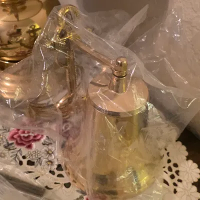 Nautical-style polished brass ship's bell mounted on an anchor bracket, wrapped in protective plastic.
