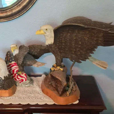 Collection of three bald eagle figurines, including a large painted resin eagle on a log base, a patriotic themed eagle with an American...