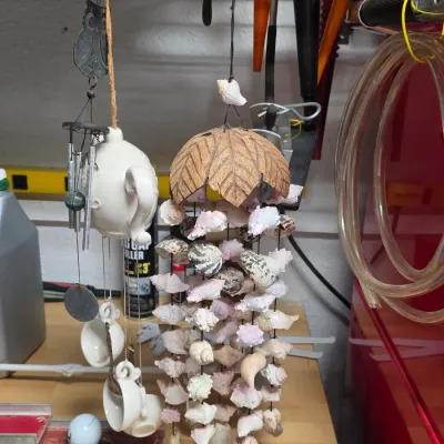 Pair of hanging wind chimes, including a large seashell wind chime with a carved coconut top and a novelty ceramic tea set wind chime.