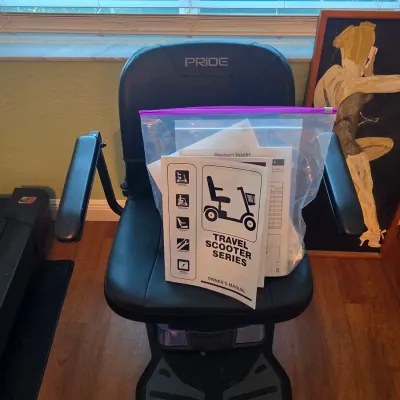 Pride Travel Scooter with black vinyl seating, padded armrests, and original owner's manual.
