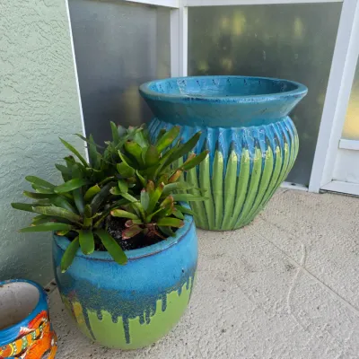 Two glazed ceramic garden planters in blue and green drip-glaze finish, including one planted with bromeliads.