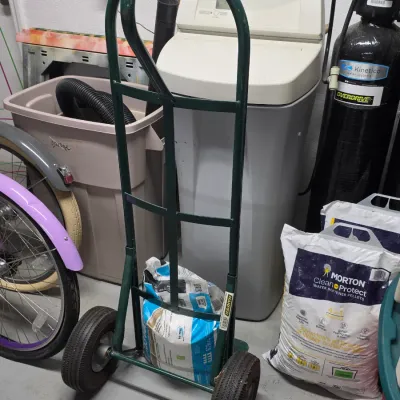 Green Harper heavy-duty hand truck trolley with pneumatic tires, resting alongside bags of water softener salt in a utility room setting.