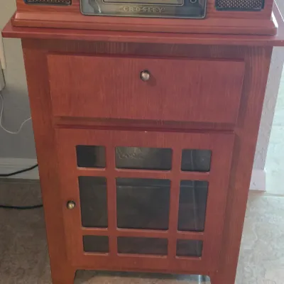 Crosley vintage-style turntable audio system seated on a matching wood media cabinet with a single drawer and glass panel door.