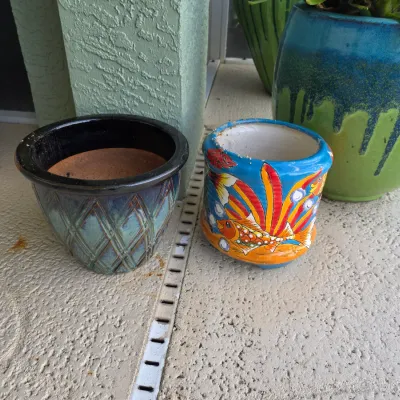 Two ceramic plant pots, including a teal glazed pot with a lattice texture and a brightly hand-painted Talavera-style pot featuring...