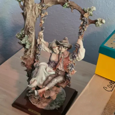 Giuseppe Armani porcelain figurine depicting a romantic couple on a swing suspended from a tree branch, mounted on a wooden display base.