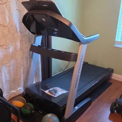 Modern Pro-Form folding treadmill with built-in touchscreen display and device holder, accompanied by a set of weighted medicine balls.