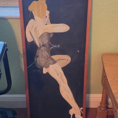 Mid-century framed artwork depicting a stylized pin-up figure set against a dark background, housed in a simple wooden frame.