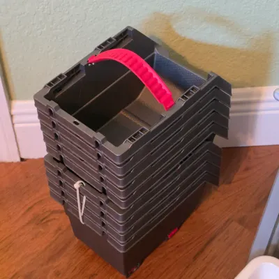 Stack of dark gray plastic storage bins featuring red carrying handles.