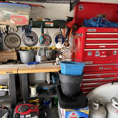 A garage or workshop setup featuring a red U.S. General rolling tool chest, a Senix walk-behind lawn mower, propane tanks, and organized...