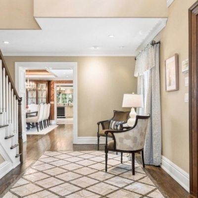 Sale Photo Thumbnail #3: Spacious home entryway featuring a dark wood front door, a grand staircase with white spindles, geometric pattern area rug, and accent armchairs.