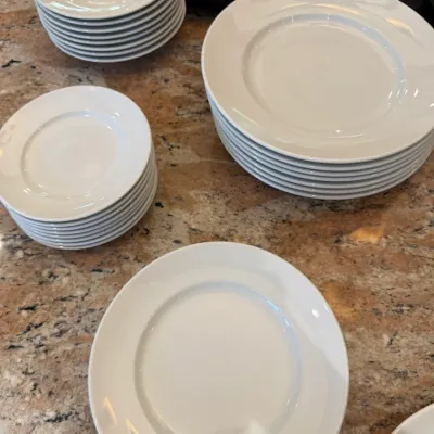 Sale Photo Thumbnail #137: Set of white porcelain dinnerware including stacks of dinner plates, salad plates, and shallow bowls arranged on a granite countertop.