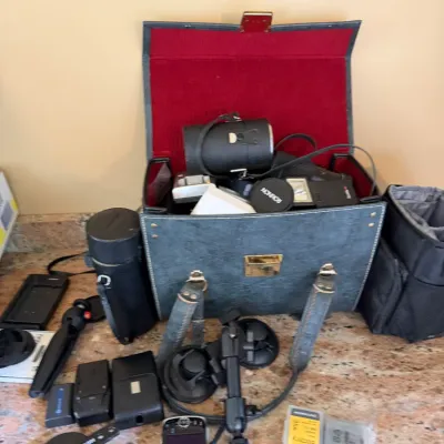 Sale Photo Thumbnail #182: Vintage camera equipment collection including a hard-sided carrying bag with red felt interior, lens cases, mini tripod, suction mount, and various accessories.
