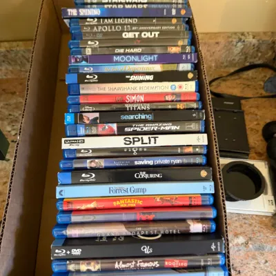 Sale Photo Thumbnail #183: Large stack of modern Blu-ray and 4K Ultra HD movies stored in a cardboard box, including popular film titles like Star Wars, Split, Forrest Gump, and Hereditary.
