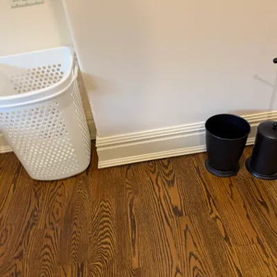 Sale Photo Thumbnail #148: White plastic tall laundry basket displayed alongside a black wastebasket and a matching freestanding toilet paper holder.