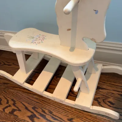 Sale Photo Thumbnail #153: Vintage white wooden rocking horse featuring hand-painted floral accents and side foot pegs.