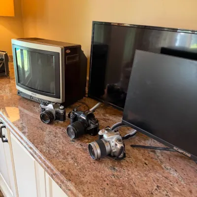 Sale Photo Thumbnail #185: Collection of electronics on a granite countertop, including a vintage Sony CRT television, flat-screen monitors, and three 35mm film SLR cameras.