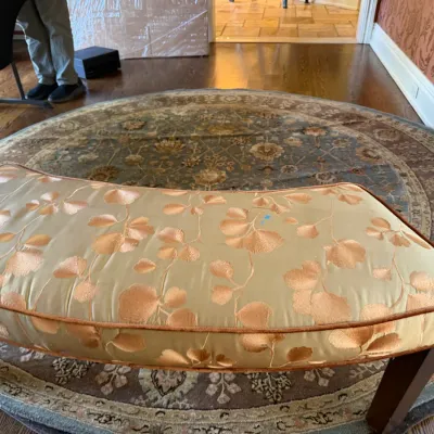 Sale Photo Thumbnail #74: Curved upholstered bench featuring a gold botanical leaf pattern, set atop a large round traditional area rug.