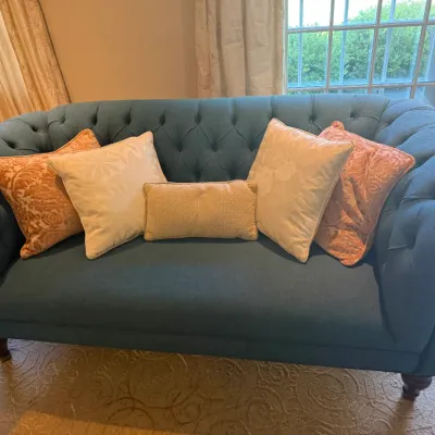 Sale Photo Thumbnail #30: Teal upholstered Chesterfield-style sofa with button tufting, rolled arms, turned wooden legs, and an assortment of throw pillows.