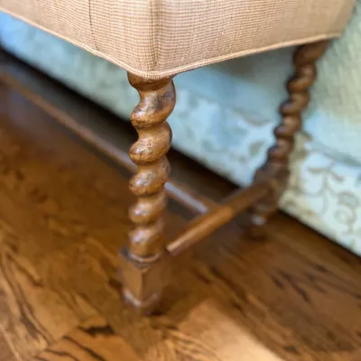Sale Photo Thumbnail #86: Detail view of an upholstered bench featuring barley twist carved wooden legs and a cross stretcher base.