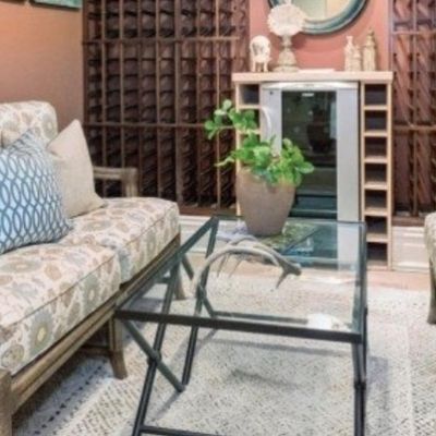 Sale Photo Thumbnail #14: Matching pair of upholstered armchairs featuring floral patterned cushions, accent pillows, and distressed wooden frames arranged around a glass-top coffee table.