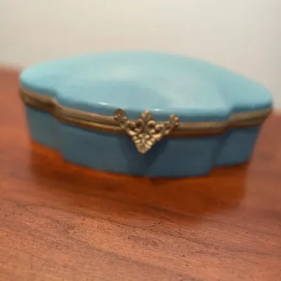 Sale Photo Thumbnail #92: Light blue porcelain trinket box with a brass filigree clasp and scalloped edges.