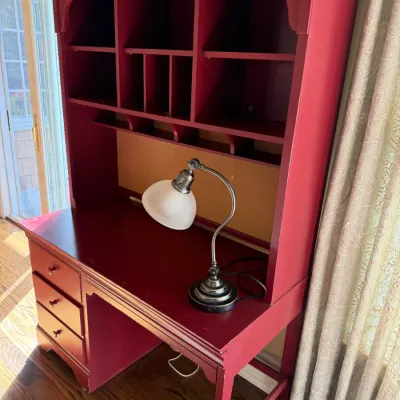 Sale Photo Thumbnail #176: Red painted wooden student desk with hutch featuring multiple cubbies and drawers, accompanied by a brushed metal gooseneck desk lamp.