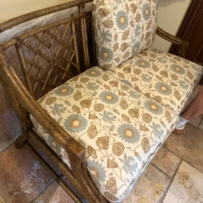Sale Photo Thumbnail #200: Faux bamboo or rattan loveseat featuring a geometric fretwork back and upholstered floral cushions in shades of blue, gold, and cream.