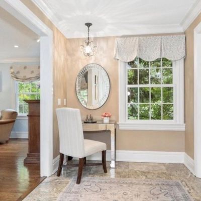 Sale Photo Thumbnail #12: Home entryway vanity nook featuring a mirrored console table, oval starburst mirror, white upholstered side chair, and small hanging chandelier.