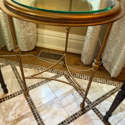 Sale Photo Thumbnail #72: Round gilt metal accent table featuring a glass insert top, three slender legs, and a tri-part lower stretcher.