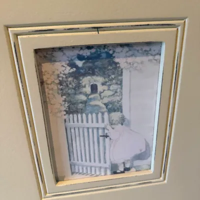 Sale Photo Thumbnail #39: Framed storybook illustration print featuring a child at a picket fence, set in a distressed cream-painted wooden frame.