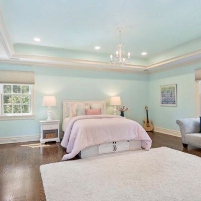 Sale Photo Thumbnail #11: Spacious bedroom featuring light blue walls, tray ceiling with crystal chandelier, a white storage bed frame, matching dresser, and a grey upholstered chaise lounge.
