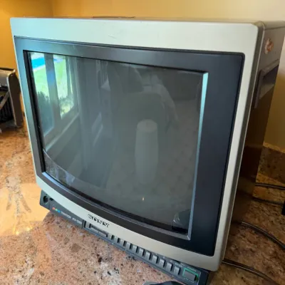 Sale Photo Thumbnail #189: Vintage Sony Trinitron KV-1365 CRT color television monitor, featuring a gray cabinet and front control panel, shown sitting on a countertop.