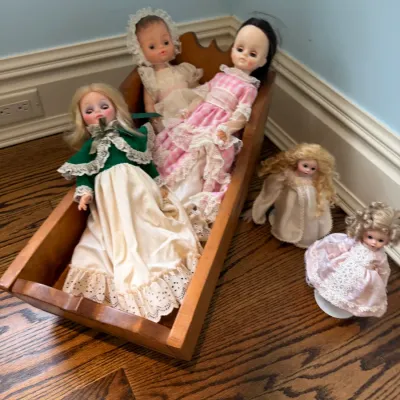 Sale Photo Thumbnail #151: Collection of vintage dolls displayed in and around a wooden doll cradle.