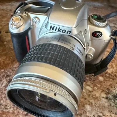 Sale Photo Thumbnail #186: Nikon N55 35mm SLR camera in silver finish, paired with a Nikon AF Nikkor 28-80mm zoom lens.