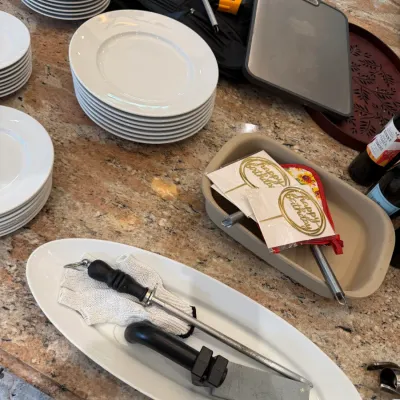 Sale Photo Thumbnail #136: Collection of kitchen items including stacks of white porcelain plates, a knife honing steel and oyster knife on a oval platter, and a Stoneware baking dish with birthday cake toppers.