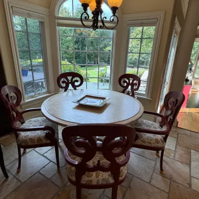 Sale Photo Thumbnail #171: Round dining table with stone top paired with five dark wood chairs featuring scrollwork backs and upholstered seats.