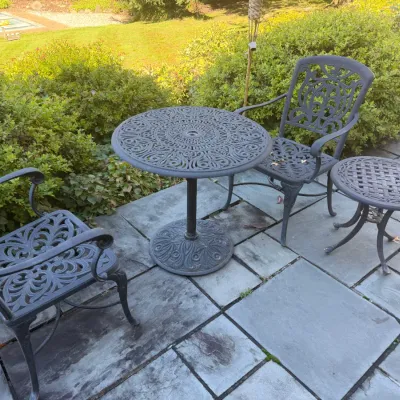 Sale Photo Thumbnail #18: Four-piece dark gray cast aluminum bistro patio set, including a round table, two ornate armchairs, and a small accent table.