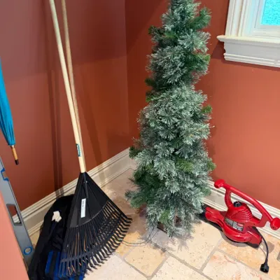 Sale Photo Thumbnail #125: Selection of lawn and home items including a plastic leaf rake with wooden handle, an artificial flocked slim Christmas tree, and a red Toro electric leaf blower.