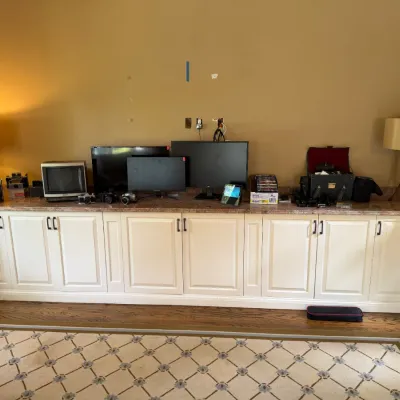 Sale Photo Thumbnail #180: Collection of vintage electronics, computer monitors, small TVs, cameras, and table lamps displayed on a long built-in white cabinet unit.