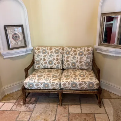 Sale Photo Thumbnail #77: Two-seat settee with a faux-bamboo wooden frame and botanical floral upholstered cushions, placed between two arched wall alcoves.