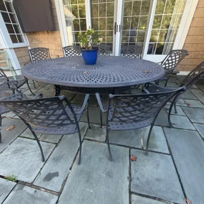 Sale Photo Thumbnail #20: Large dark grey cast aluminum outdoor patio dining set, featuring a round lattice-top table and matching armchairs.